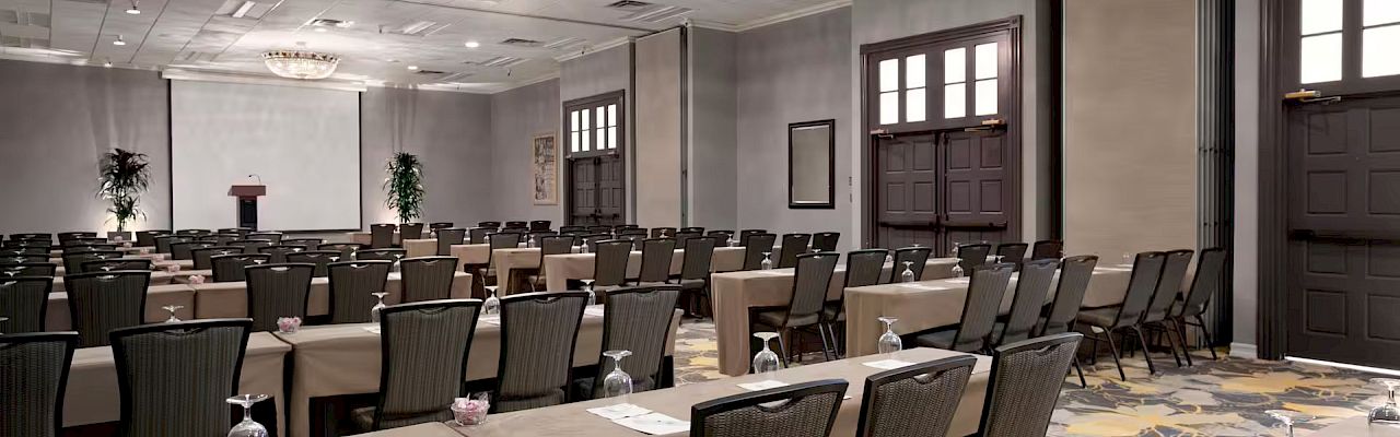 The image shows a conference room setup with rows of tables and chairs facing a podium, ready for a presentation or meeting.