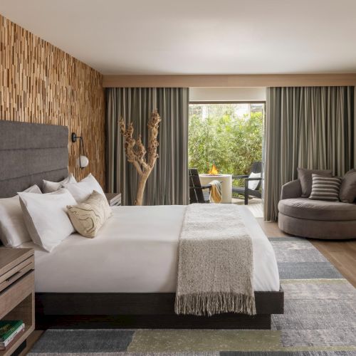 Modern hotel room with a king bed, wood-paneled feature wall, nightstands, a cozy chair, dresser, and a balcony view.