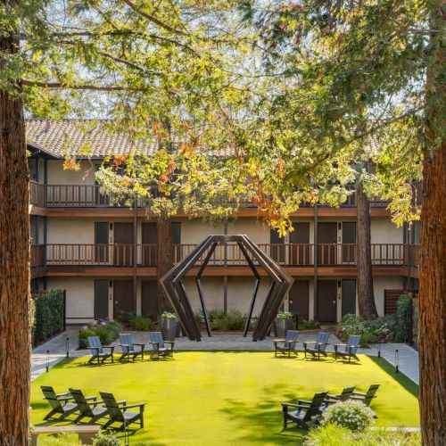 A cozy wooden cabin in a sunny yard, surrounded by trees and a few outdoor chairs.